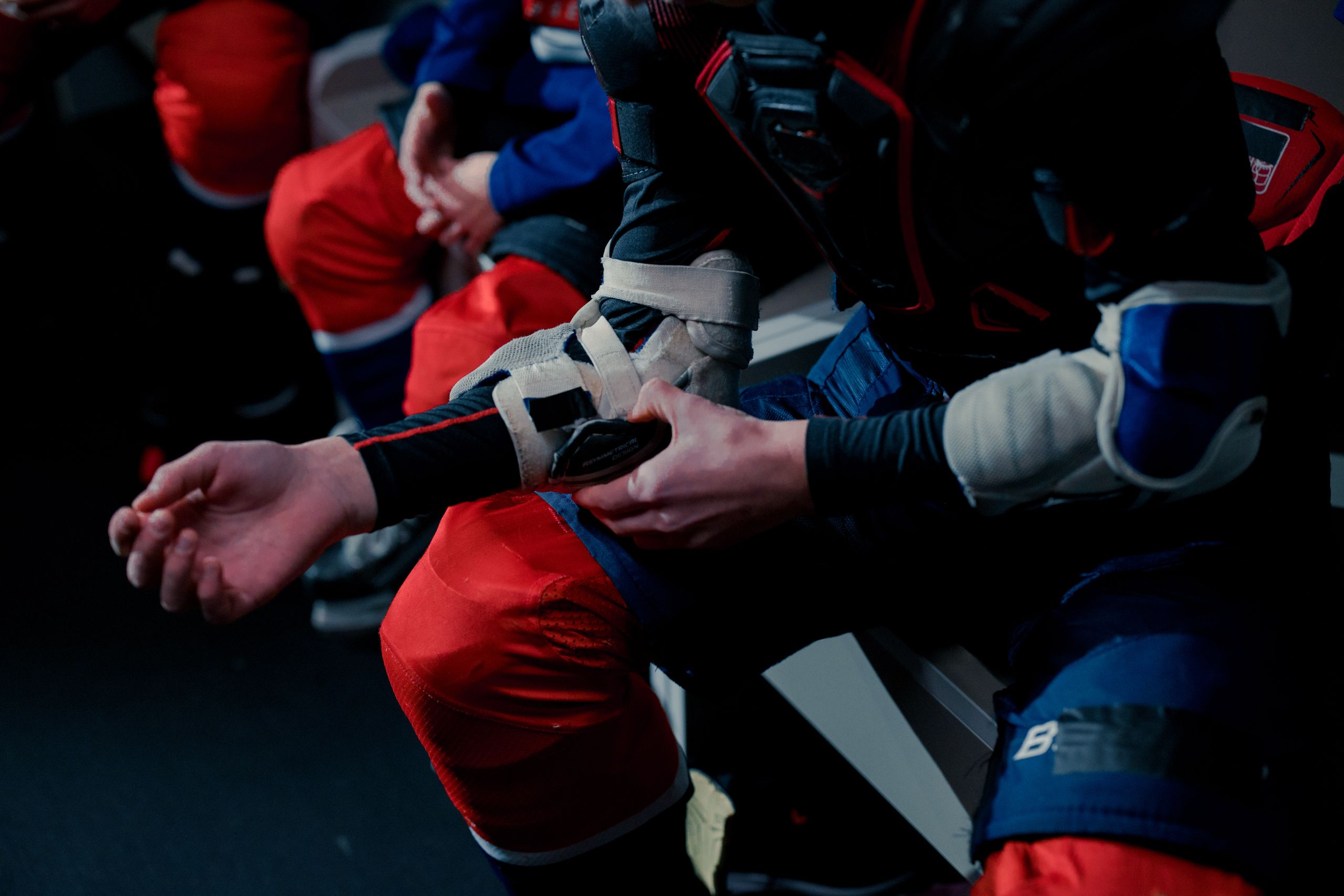 Teen hockey players getting ready in a locker room, adjusting safety gear and shoulder pads.